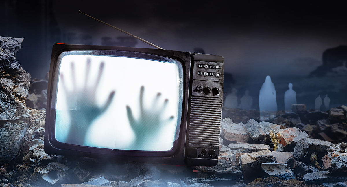 Horror photo of an old black scary haunted tv set with ghost hands on screen, standing on dark foggy ruined city with spirit figures background. Foto: Shutterstock