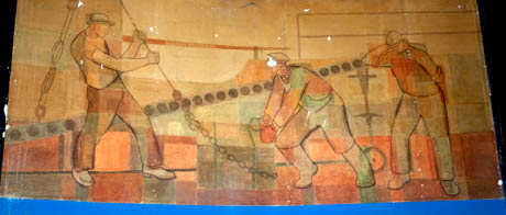 Tre tunga betongklumpar med motiv från hamnarbetarnas vardag. Den vänstra hamnarbetaren har bevarats av Stadsmuseet i Stockholm.