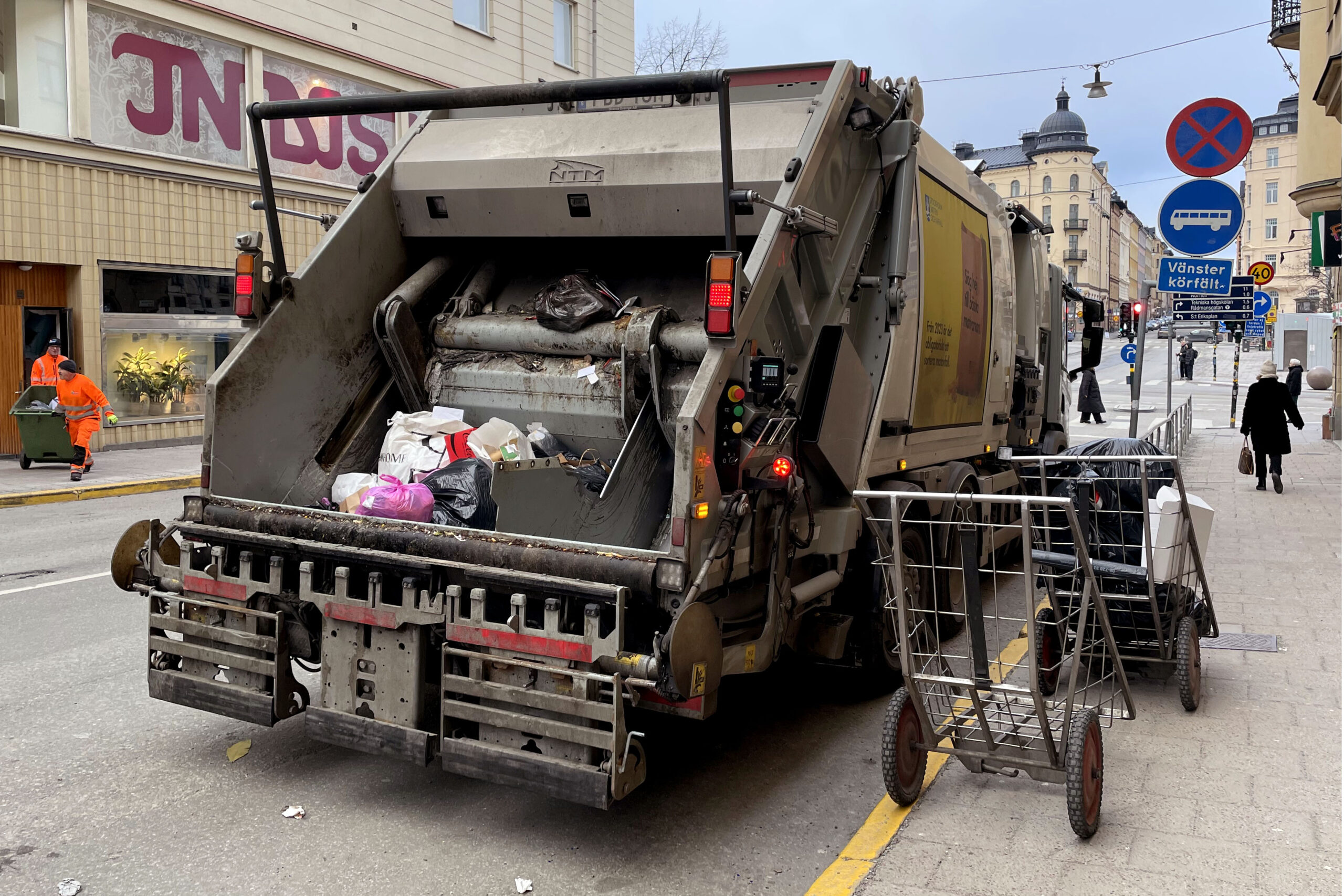 Arkivbild. Sopbil på gata i Stockholm med två sopgubbar och en gående.